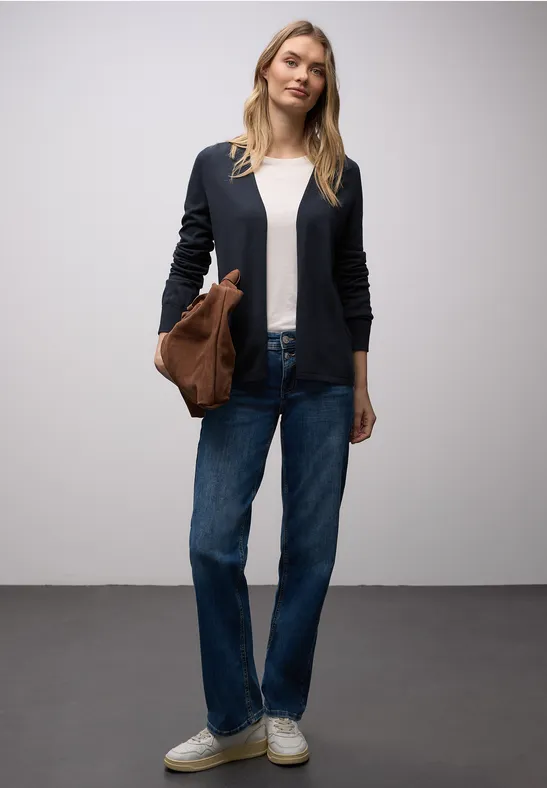 Person trägt dunkelblauen Blazer, weißes Shirt, gerade geschnittene Jeans, weiße Sneaker und braune Tasche.