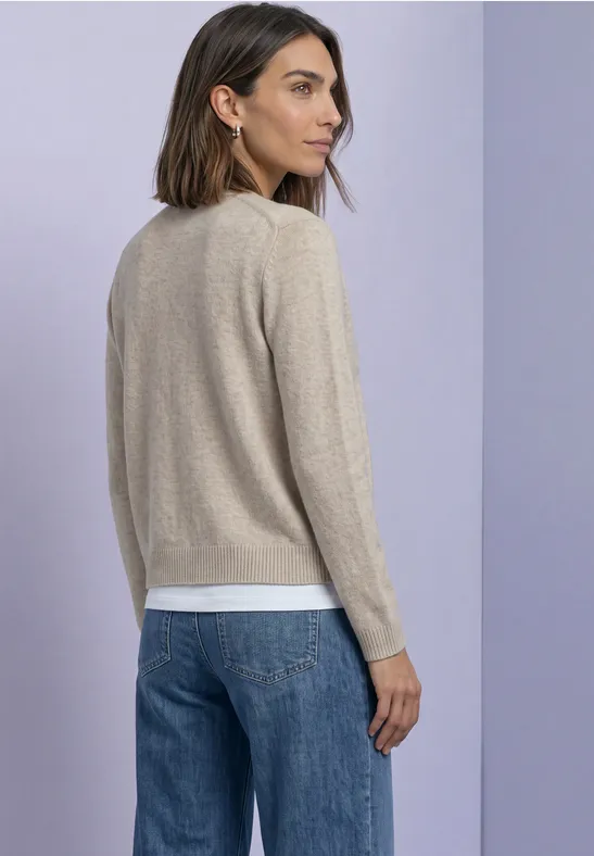 Rückansicht einer Frau mit beigem Pullover, weißem Shirt und blauer Jeans vor lila Hintergrund.