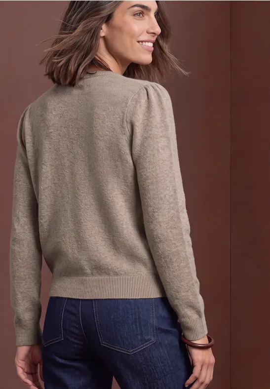 Rückansicht einer Frau mit beigem Strickpullover, Jeans und kurzem braunem Haar vor braunem Hintergrund.