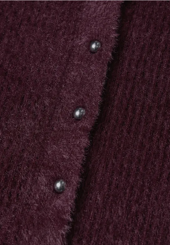 Nahaufnahme eines weinroten, flauschigen Strickcardigans mit Rippenstruktur und glänzenden Knöpfen.