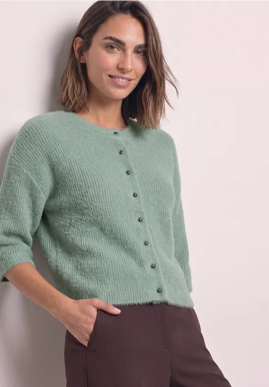 Femme portant un gilet court vert menthe boutonné et un pantalon marron, main dans la poche