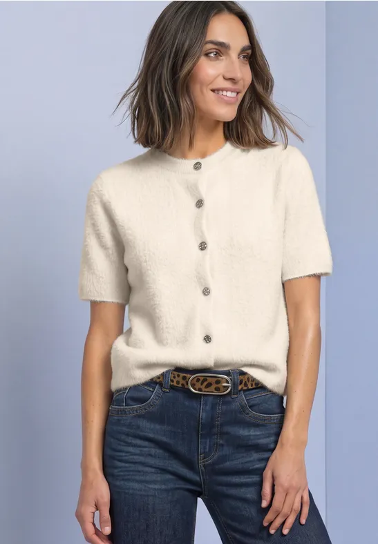 Vrouw draagt crème kort mouw gebreid vest met knopen, jeans en riem