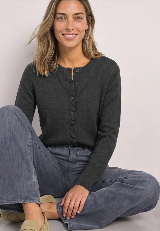 Femme assise en tailleur, vêtue d'un gilet gris foncé et d'un jean.