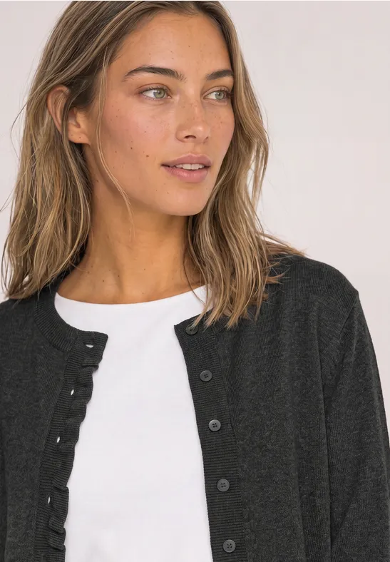 Femme aux cheveux bruns portant un top blanc et un cardigan noir, regard de côté.