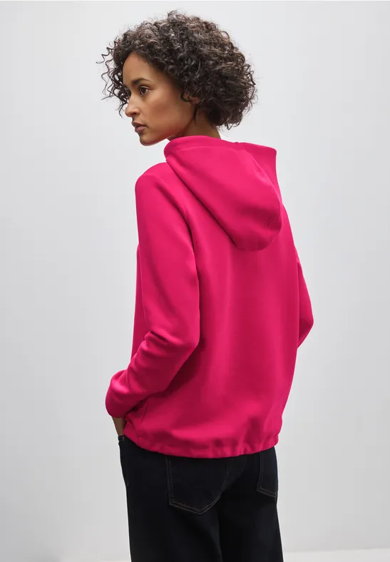 Frau mit pinkem Kapuzenpullover und blauer Jeans von hinten.
