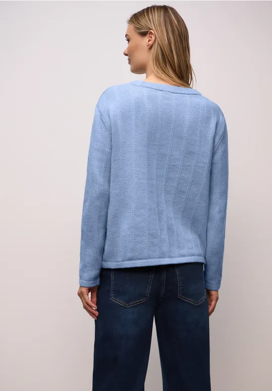 Dame trägt skyblaues langärmeliges Shirt und dunkle Jeans vor hellem Hintergrund