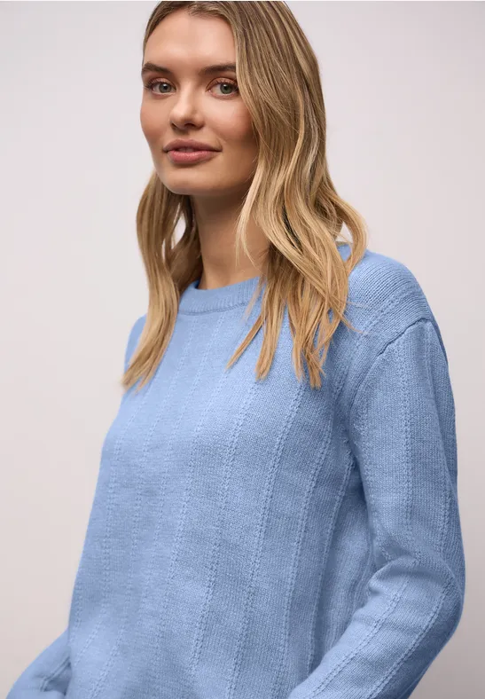 Frau mit langen blonden Haaren trägt einen hellblauen Strickpullover.