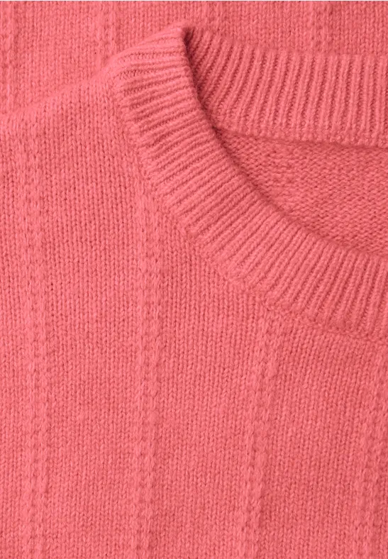 Nahaufnahme eines korallenroten Strickpullovers mit Rundhalsausschnitt und Zopfmuster.