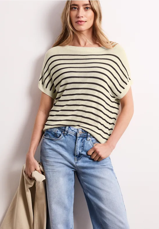 Frau trägt gestreiftes T-Shirt und Jeans, hält Mantel in der Hand.