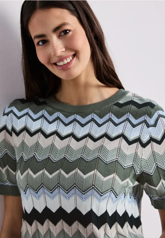 Vrouw draagt een T-shirt met korte mouwen en zigzagpatroon in groen-, lichtblauw-, zwart- en wit tinten.