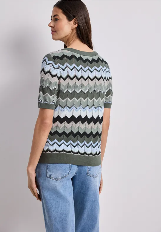 Vrouw van achteren in een top met zigzagpatroon in groen, zwart, lichtblauw en een spijkerbroek.