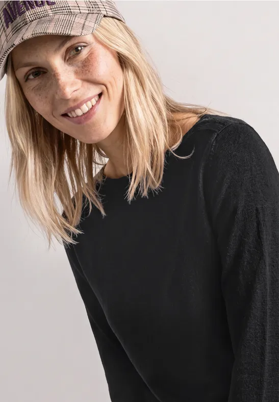 Eine lächelnde Frau mit Baseballcap und schwarzem Pullover vor neutralem Hintergrund.