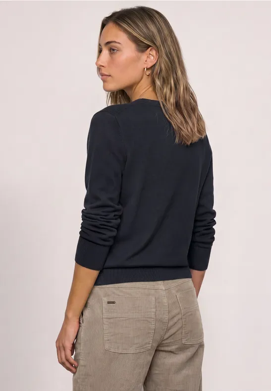 Rückansicht einer Frau in einem dunkelblauen Pullover und beigen Hosen.