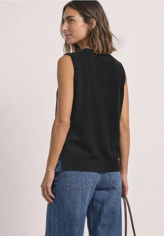 Frau in schwarzem ärmellosem Oberteil mit Jeans und brauner Tasche, seitliche Ansicht.