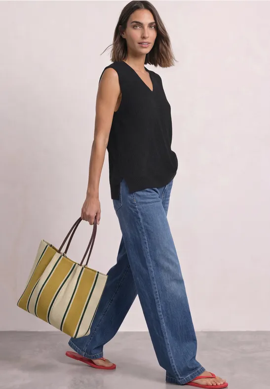 Eine Frau in schwarzem Top und weiten Jeans trägt eine gestreifte, gelb-grüne Tasche.