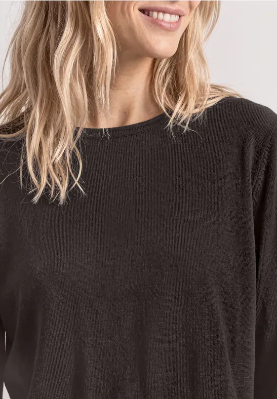 Een glimlachende vrouw met blond haar in een zwart shirt, van nek tot heup zichtbaar.