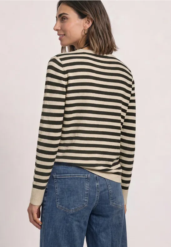 Une femme vue de dos porte un pull rayé noir-beige et un jean bleu sur un fond clair.