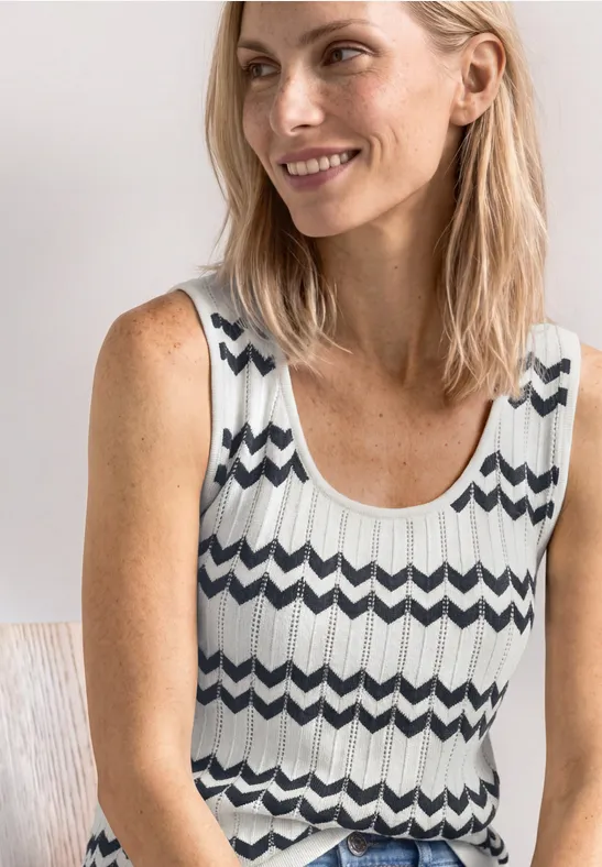 Une femme souriante portant un top sans manches noir et blanc à motif zigzag.