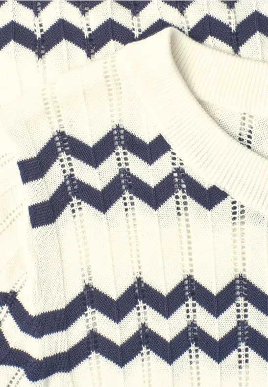 Gros plan d'un pull blanc en tricot avec des rayures en zigzag bleu marine.