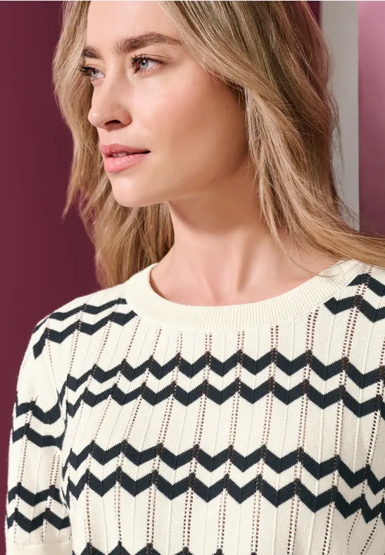 Femme portant un pull tricoté clair à motif zigzag foncé, regard de profil vers la droite.