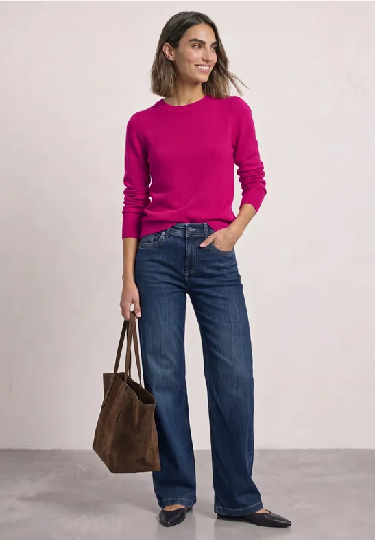 Frau in pinkem Pullover und weiten Jeans trägt braune Tasche.