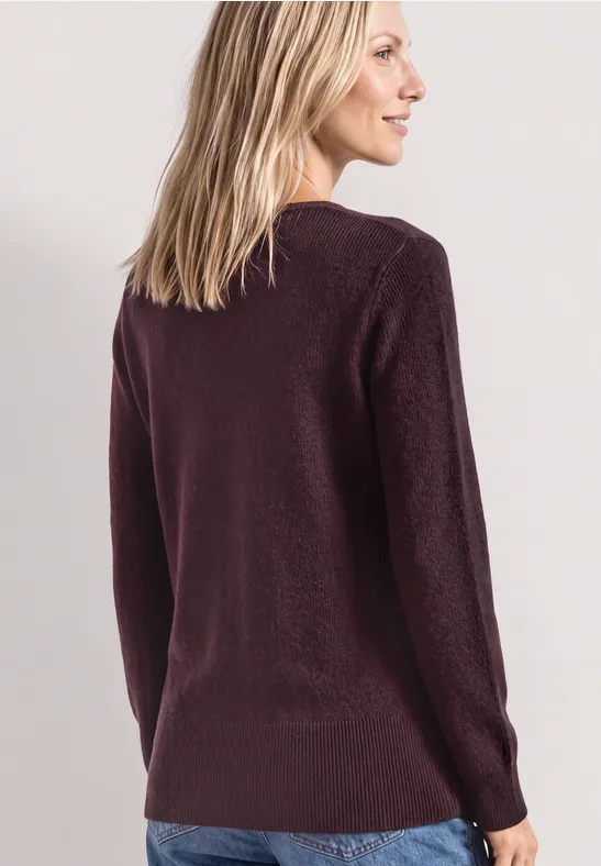 Frau von hinten in lila Pullover und Jeans, Blick seitlich nach rechts.