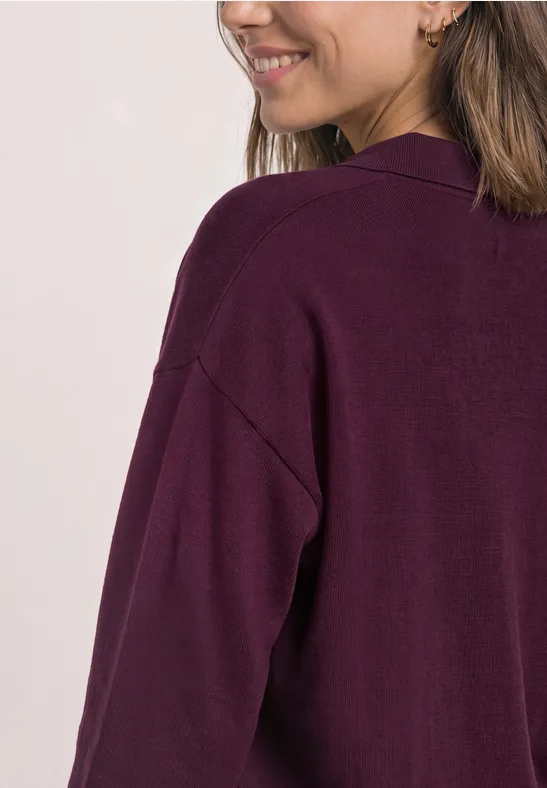 Femme de dos/latérale portant un cardigan violet foncé, souriante, épaules visible.