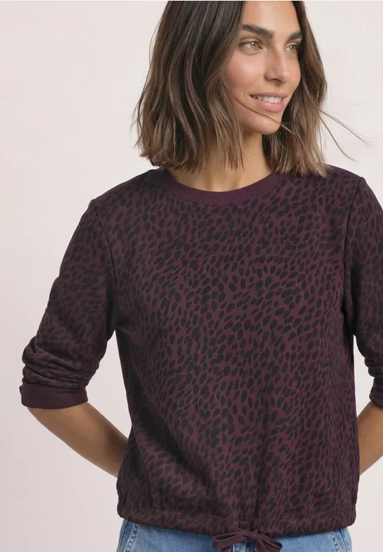 Femme en pull violet foncé à motif, noué à la taille, style décontracté et moderne.
