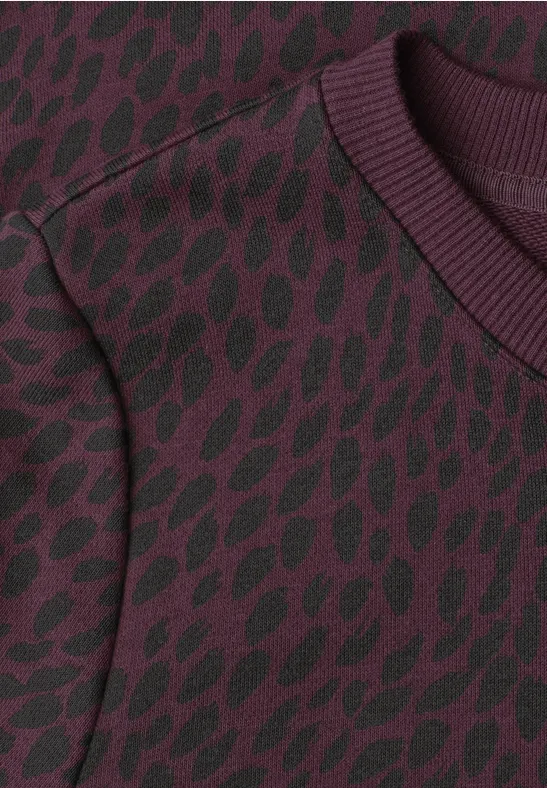Pull bordeaux à motifs de feuilles noirs et col rond côtelé.