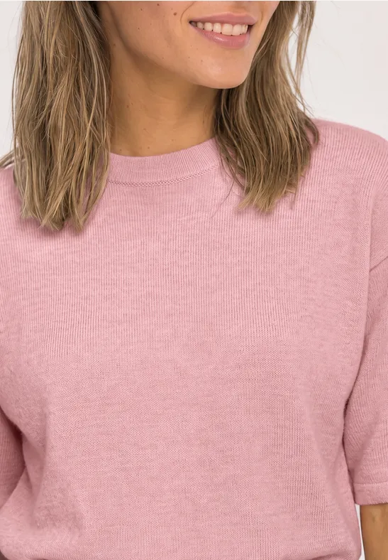 Femme en t-shirt rose aux cheveux mi-longs, sourire discret.