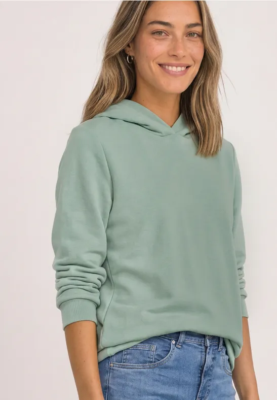 Femme souriante portant un sweat à capuche vert et un jean