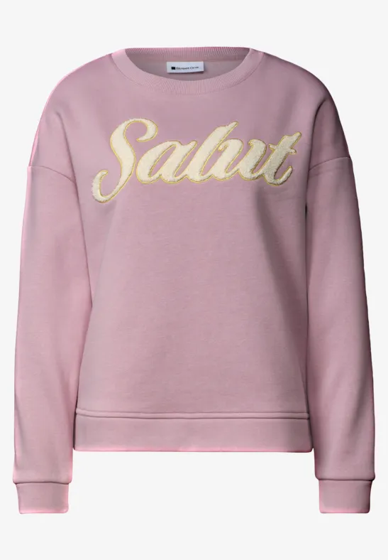 Sweat rose avec lettrage jaune «Salut» en cursive.