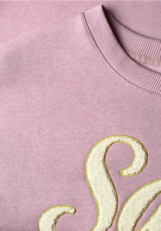 Pull rose avec motif lettre dorée pailleté, gros plan.