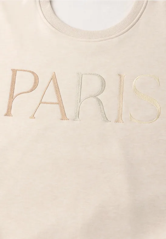 T-shirt beige arborant l’inscription PARIS en grandes lettres élégantes.