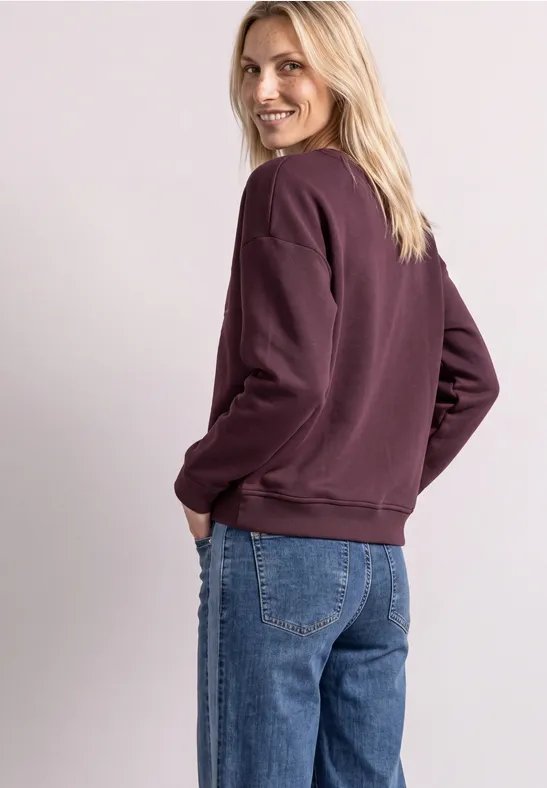 Femme en sweat violet et jean se retourne en souriant.