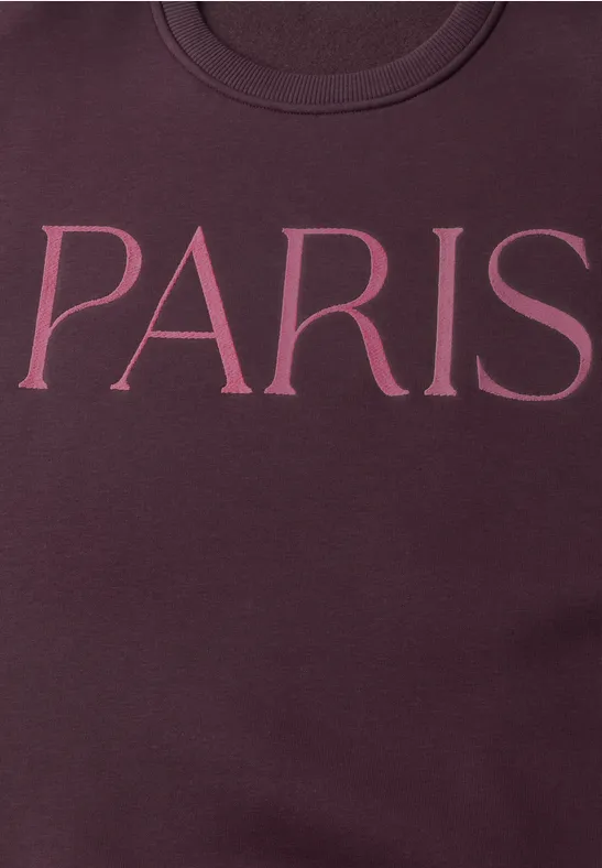 Gros plan d'un sweat bordeaux avec l'inscription 'PARIS' en lettres roses.