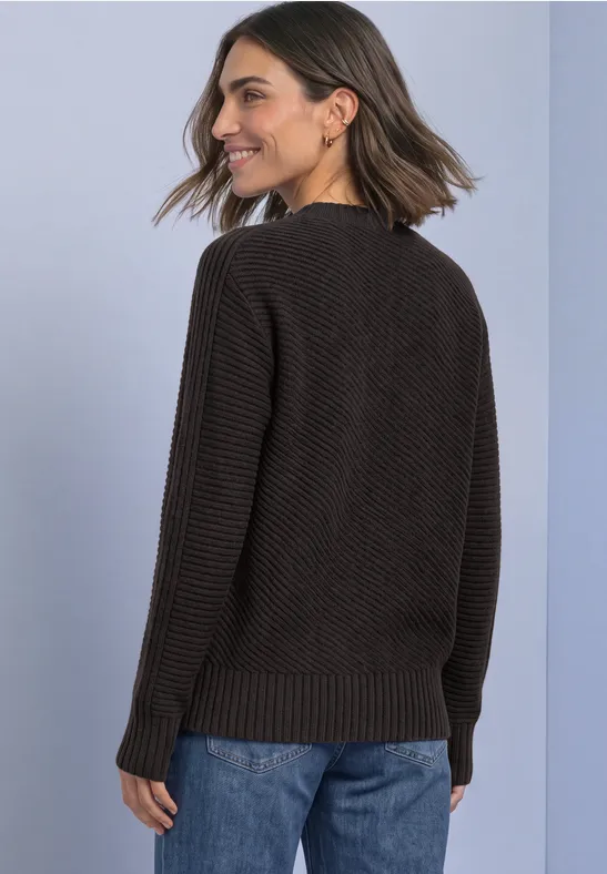 Vrouw van achteren in een zwarte gebreide trui en blauwe jeans, halflang haar, glimlachend.