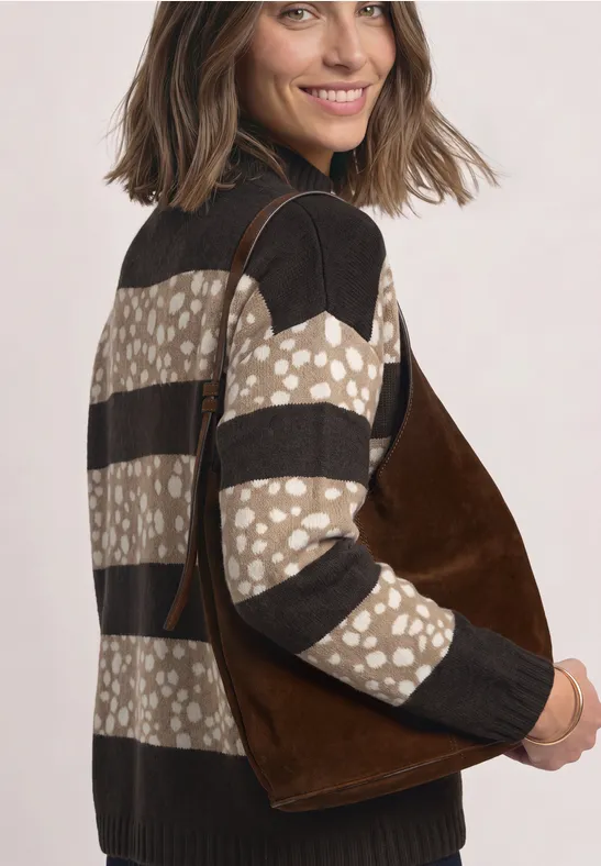 Vrouw met een bruin suède tas en een gemêleerde trui, die over haar schouder kijkt.
