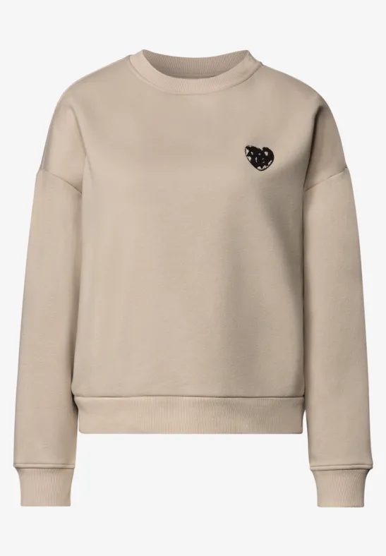 Sweat-shirt beige épuré à col rond, petit emblème cœur noir sur la poitrine.