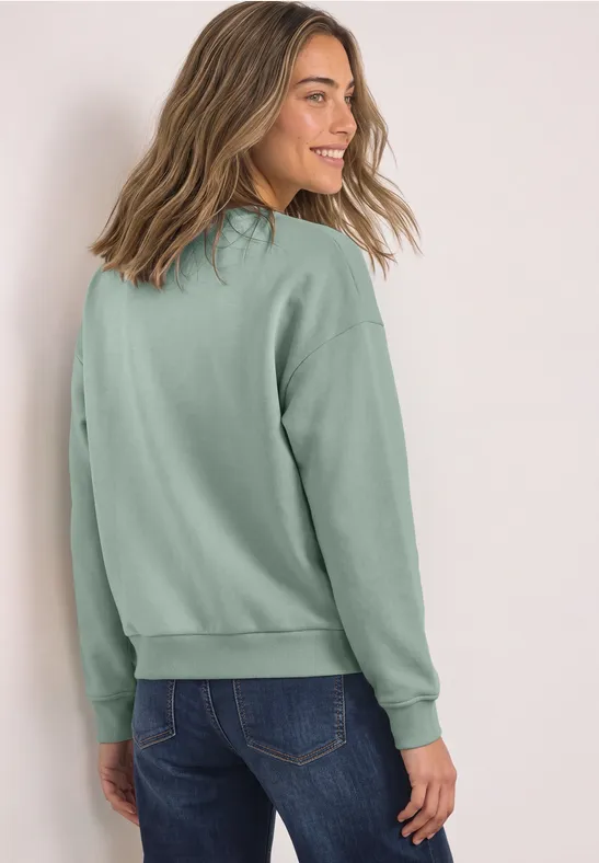 Une jeune femme en sweat vert clair sourit en se retournant.
