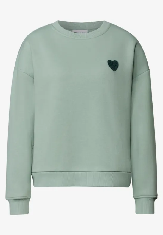 Un sweat vert menthe avec un petit cœur noir sur la poitrine.