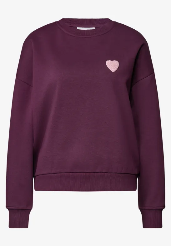 Pull violet foncé à manches longues, bords-côtes et petit cœur rose sur la poitrine.