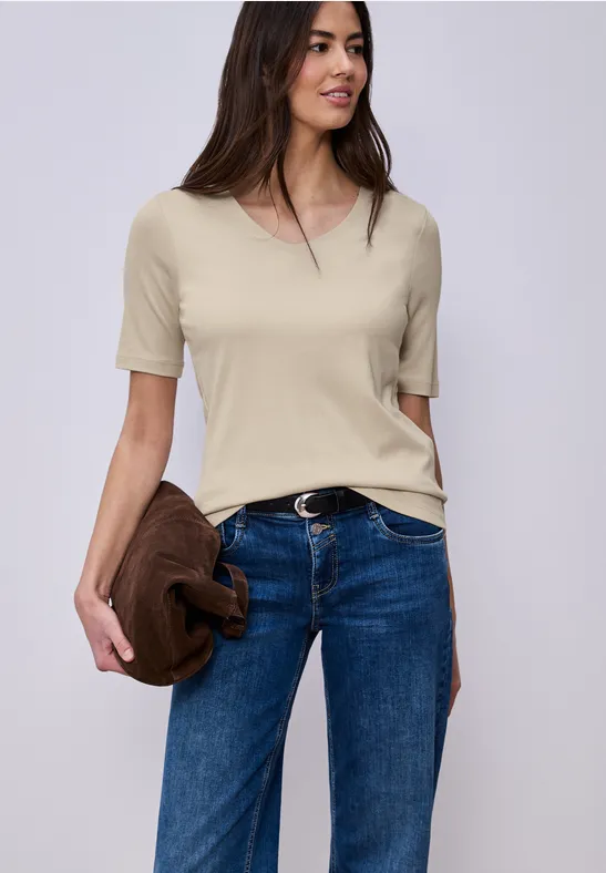 Persoon in beige T-shirt en blauwe jeans houdt nonchalant een bruine jas vast