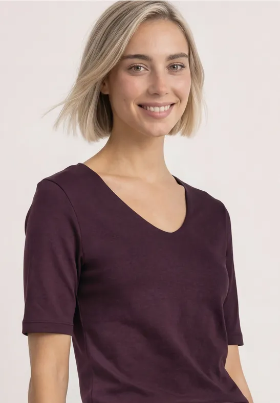 Junge Frau mit kurzem blonden Haar und lila T-Shirt lächelt vor hellem Hintergrund.
