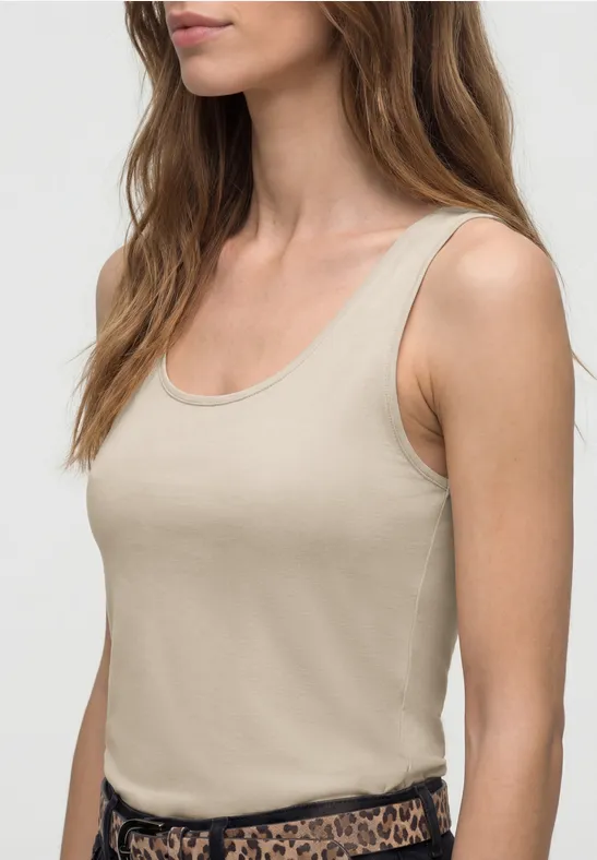 Frau im beigen Tanktop, seitliche Ansicht von Oberkörper und Haaren vor neutralem Hintergrund.