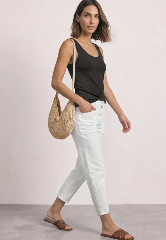 Frau in schwarzem Top und weißen Hosen trägt braune Sandalen und eine Strohtasche.
