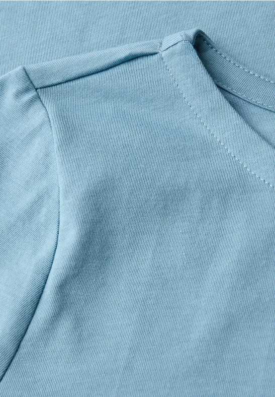 Gros plan d’un t-shirt bleu clair en coton avec couture apparente à l’épaule et à l’encolure.