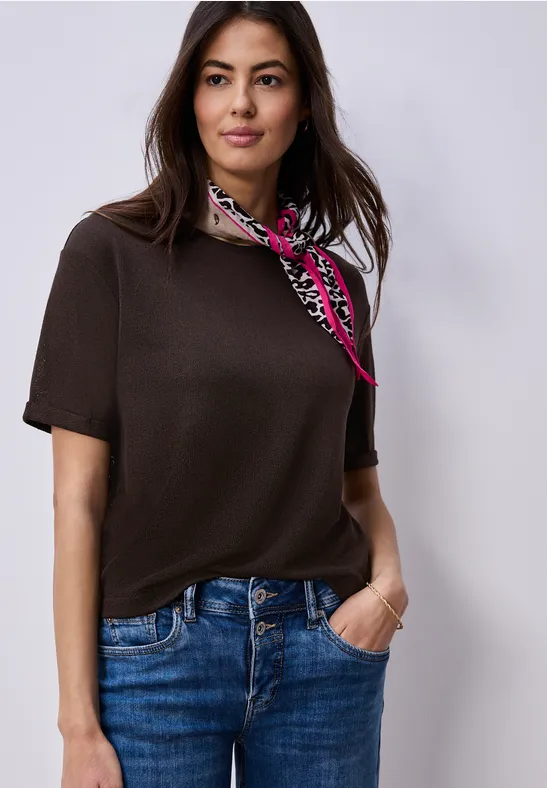 Femme portant un top marron à manches courtes, un jean bleu et un foulard à motifs.