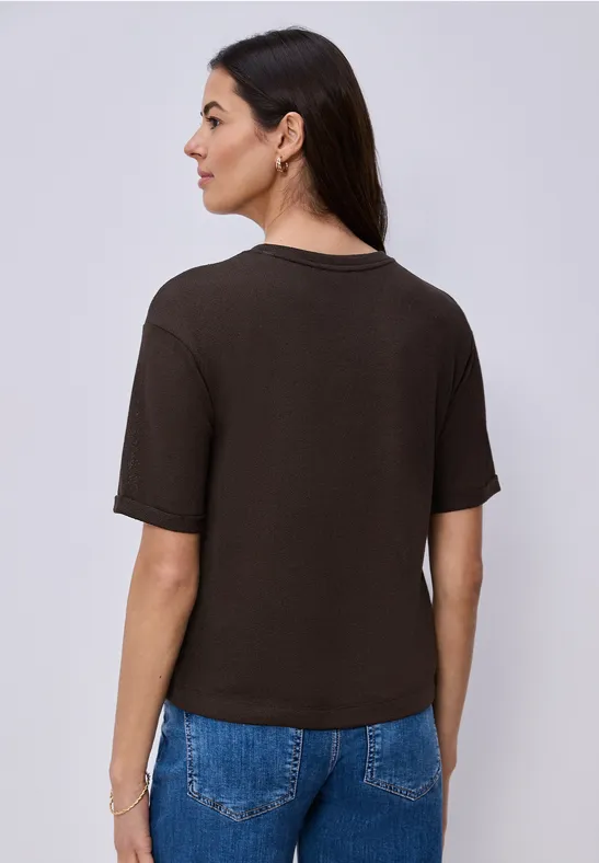 Une femme vue de dos, portant un t-shirt noir sobre et un jean bleu sur un fond clair.