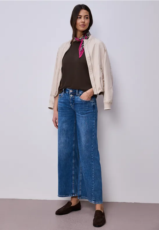Femme en veste blanche, top marron, foulard rouge, jean large bleu et mocassins noirs.
